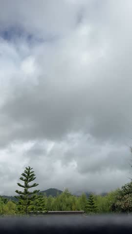 A cloudy sky with slow-moving clouds above a beautiful mountain range covered in green trees. A tranquil and peaceful nature scene.