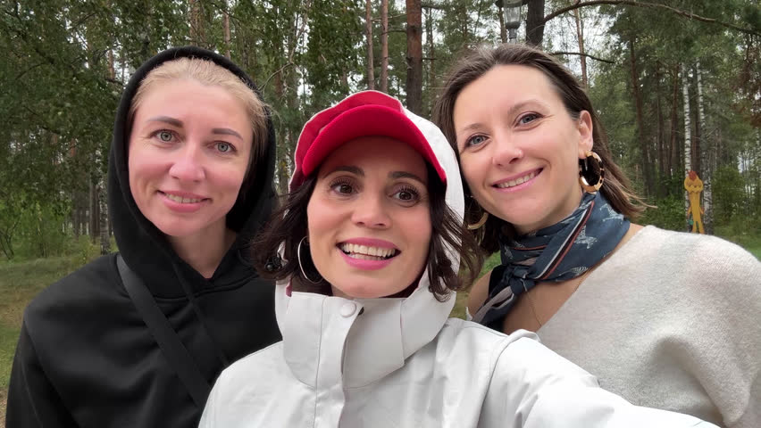 Three happy women waving at camera in forest, cheerful female friends enjoying outdoor walk in nature, autumn mood and friendship