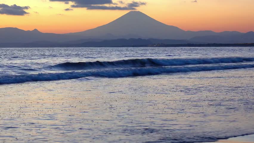Mount fuji rises above the horizon over the ocean at sunset