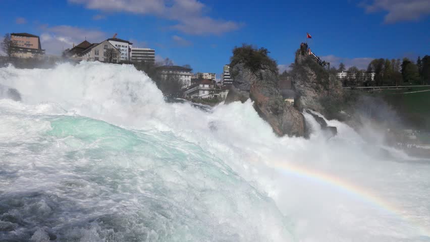 Water falls and drops scatter in different directions on Rhine Falls against old town in Switzerland
