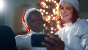 Happy multiethnic spouses celebrating Christmas, calling by video to friends. Portrait of african american husband and caucasian wife in Santa hats on head, modern technology for communication online - Powered by Shutterstock - Get 15% off with code: PIKWIZARD15