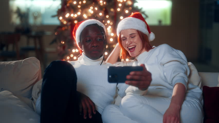 Merry Christmas and happy new year, biracial couple relaxing at home in night. Joyful young woman and man surfing internet by smartphone, modern technology and traditional celebration winter fest - Powered by Shutterstock - Get 15% off with code: PIKWIZARD15