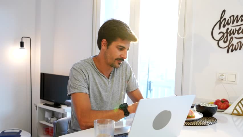 Young male freelancer concentrating on his laptop, enjoying a productive work from home experience in his modern apartment