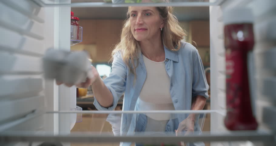 Inside Fridge POV: Woman Carefully Organizes Groceries in the Fridge after doing Groceries Shopping, Arranging Milk, Eggs, and Fresh Vegetables. After Shopping, She Plans a Nutritious Meal for Family