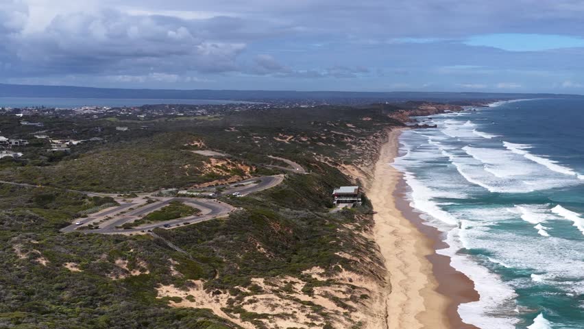 Drone glides above Portsea coastline, revealing cliffside building, sandy beach, and rolling ocean waves - Powered by Shutterstock - Get 15% off with code: PIKWIZARD15