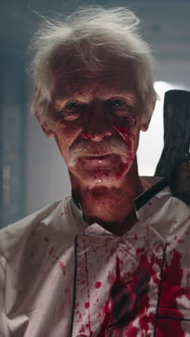 Close up of creepy bloody man with grey hair laughing insanely holding axe on shoulder standing in dark haunted corridor cinematic horror slow motion scary halloween slasher atmosphere