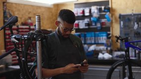 Professional bicycle mechanic wearing protective apron and glasses working with smartphone inside workshop, managing customer interactions and business operations using mobile technology - Powered by Shutterstock - Get 15% off with code: PIKWIZARD15