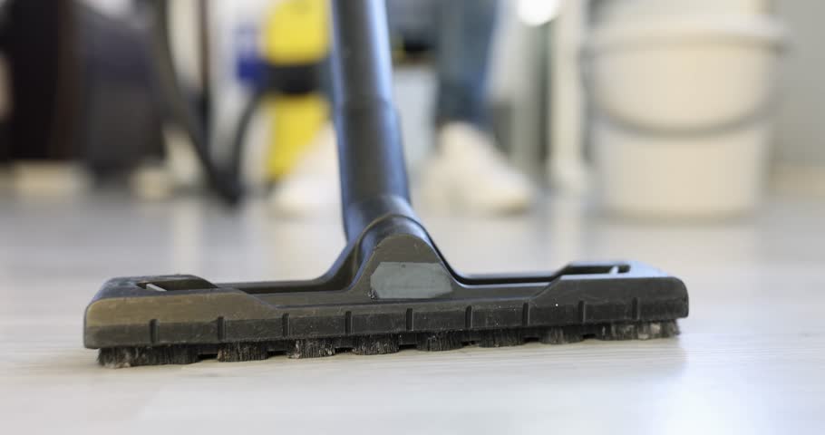 Head of black vacuum cleaner on light-colored laminate floor. Cleaning emphasizes detail of tool bristles and task of maintaining tidy setting