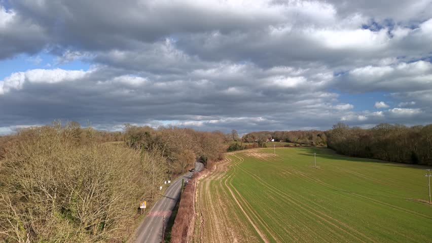 Aerial view rising over sunny Autumn English farmland countryside under grey rainy clouds