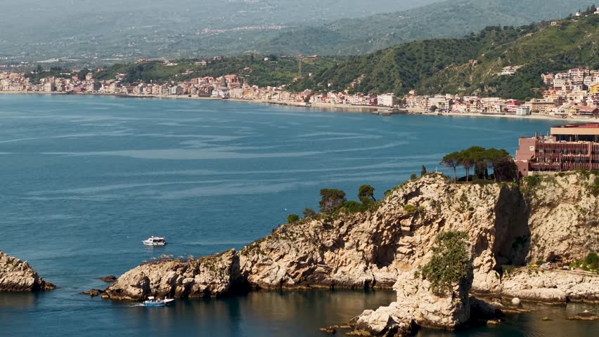 Establishing aerial view of Isola Bella island with boats sailing the rocky sunny Italian coast