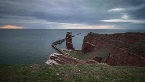 Timelapse of sunset over Heligoland in North Sea with shifting colors of sky, glowing reflection of sun on the water, and changing light on sandstone cliff and rock formation "Lange Anna."  - Powered by Shutterstock - Get 15% off with code: PIKWIZARD15