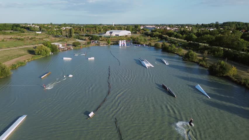 Drone footage captures Lac de Saujon in Charente-Maritime, highlighting the téléski nautique station with riders gliding across the lake’s surface under the sun.