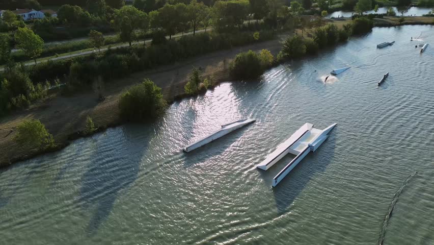A dynamic drone footage shows Lac de Saujon in Charente-Maritime with people riding on water at the téléski station, framed by the natural charm of the surrounding landscape.