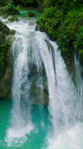 Aerial multi-tiered waterfall cascades into turquoise pools amidst green tropical foliage. Kawasan Falls, Philippines.