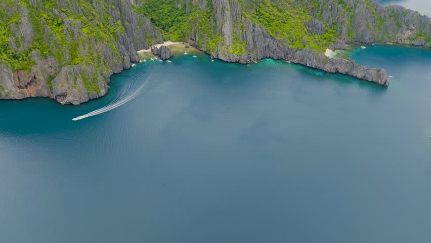 Boats and white sand beach in Secret Lagoon and Jijis Beach. Top view of tropical island surrounded by blue sea. El Nido, Philippines.