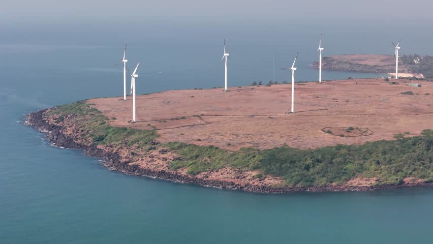 Aerial view of a coastal wind farm with wind turbines generating renewable energy on a cliff by the sea in Devgad, India.