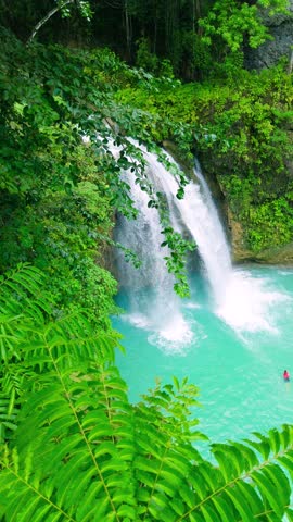 Aerial view of a multi-tiered waterfall cascading into bright turquoise pools, surrounded by lush green tropical forest, Kawasan Falls, Philippines.