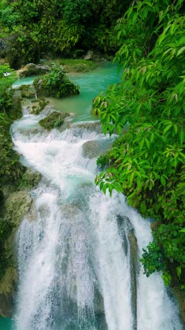 Aerial view of the multi-tiered Kawasan Falls, with turquoise water cascading into natural pools amidst lush tropical jungle, where adults are swimming, Philippines.