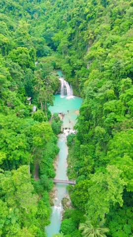 Aerial of people swimming in turquoise pools and a multi-tiered waterfall, surrounded by green jungle, Kawasan Falls, Philippines.