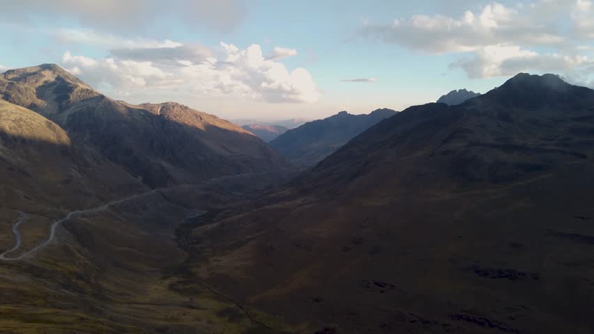 High mountain ridges and valley with a winding road appear under evening light near Cusco, Peru, Sacred Valley region, view from Amparaes high altitude point