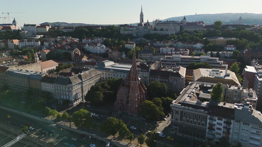 Aerial of Szilágyi Dezső Square Reformed Church in Budapest, Hungary, highlighting its red-roofed spire with the Fisherman’s Bastion framing the backdrop