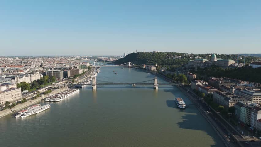 Smooth forward drone flight over Budapest’s Danube River, gliding across the Széchenyi Chain Bridge with the historic Buda and Pest skyline in view.