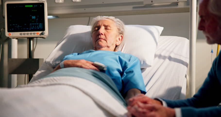 Medical, coma and senior couple in hospital with bed, support for patient in post operative care. Healthcare, sleeping and elderly people at bedside with heart monitor, diagnosis and worry in ICU.