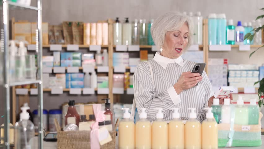 Elderly woman scans the barcode of the paracetamol package on her phone and pays for goods at the pharmacy using an online application. Pensioner pays for purchases with modern payment methods. High