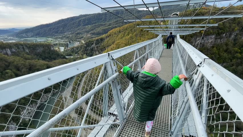 A girl walks on a suspension bridge over a canyon