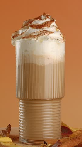 Glass straw is inserted into a glass of pumpkin latte with cream and spices.