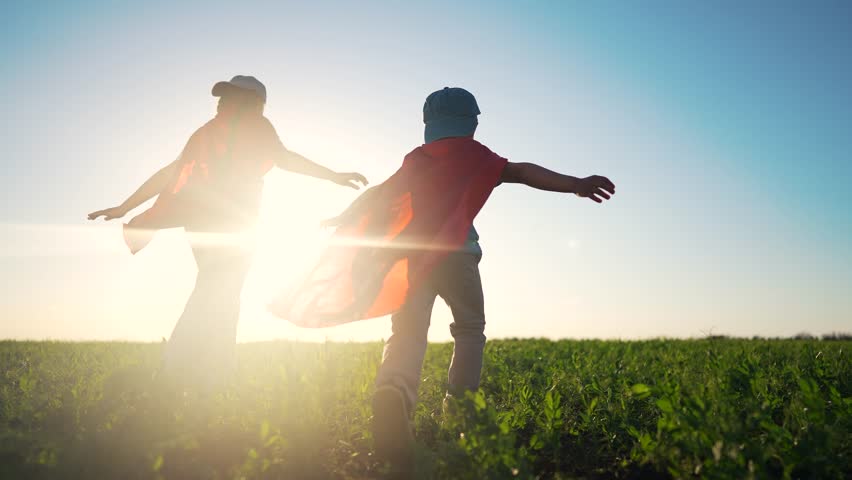 Two children in red superhero costumes running through a field. Children running in the field with superheroes. A young girl plays with her imagination in the sunlit outdoor adventure. Two lifestyle.