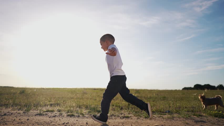 Boy running in field. Boy running in the sunlight outside. A grassy green grass in summertime nature with a shady shade. A child sprinting through a meadow lifestyle.