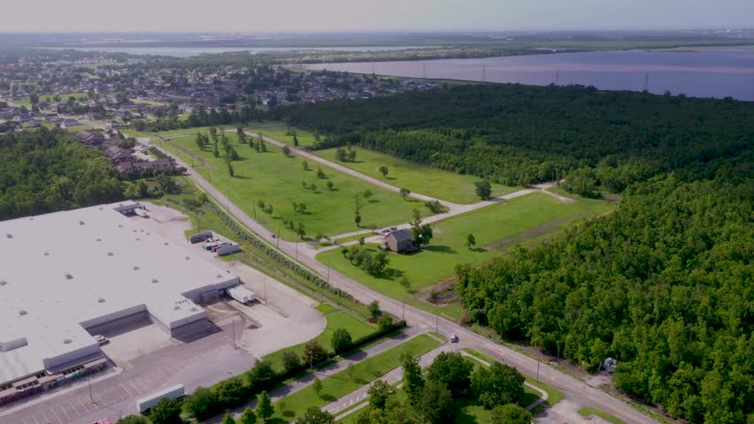 Aerial footage tracking Patricia Street in Chalmette, Louisiana, showing retail buildings, cars, the Mississippi River, houses, and the 40 Arpent Wetlands in the distance.