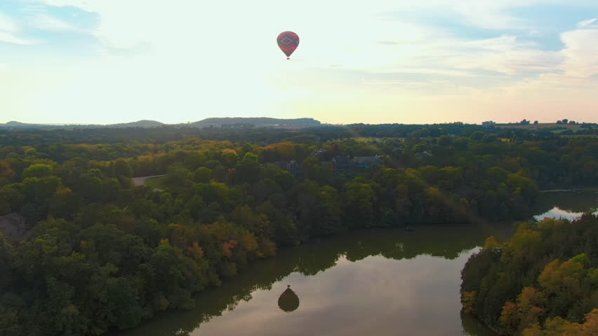 Stunning Aerial View of a Hot Air Balloon Over a Reflective Lake and Luxury Forest Homes at Sunset
