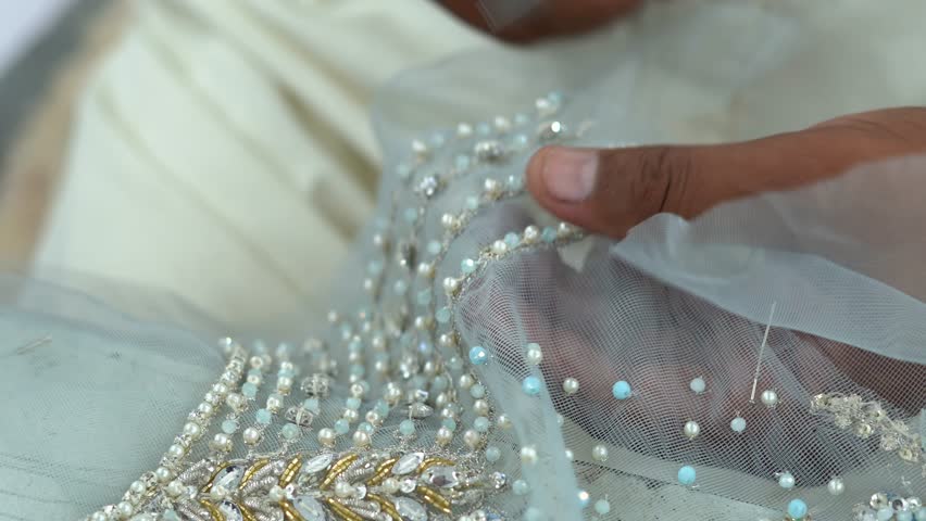 Close Up Shot Of A Dressmaker Cutting Textiles During Beading Process In A Clothing Plant In Pakistan.