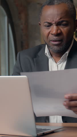 Stressed African American business man with documents headache problem job in office upset failure paperwork businessman male executive suffering with laptop report incorrect data papers dissatisfied