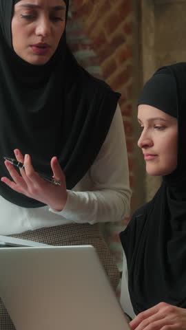 Two business women office team Muslim mentor leader company CEO with folder businesswomen consulting talking to girl intern worker corporate advice mentoring islamic female with laptop internship job