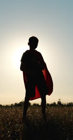 Kid superhero dances at sunset in open field. Child hero in red cape moves with joy and confidence. Young hero in mask and does playful steps. Vertical video. dance child silhouette