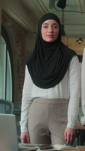 Two Muslim business colleagues team confident Islamic women in hijab partners smiling businesswomen girls project managers looking at camera in office crossed hands leaning backs partnership teamwork