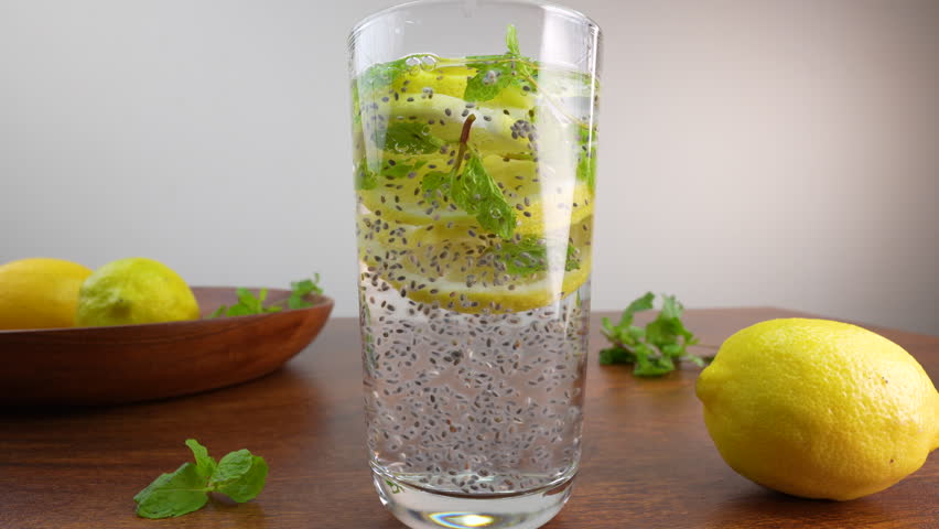 A glass of detox water with mint, lemon slices, and chia seeds, placed on a wooden table near a lemon