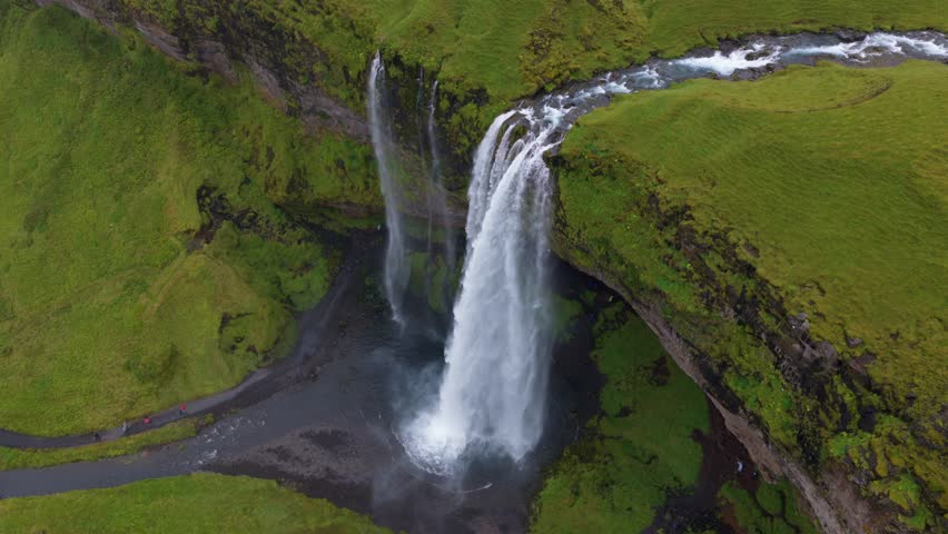 Aerial view of Seljalandsfoss waterfall in Iceland, showing its powerful flow, lush green terrain, winding river, and dark rock formations.
