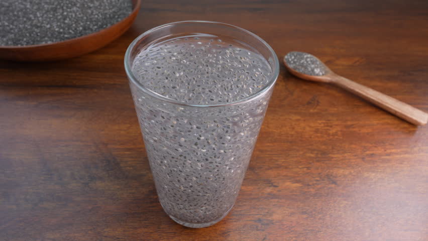 A glass of soaked chia seeds in water forming a gel-like texture, placed on a wooden table