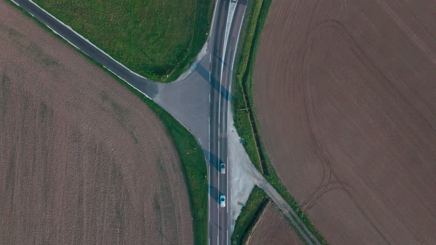 Aerial view of rural intersection with moving vehicle in countryside landscape.