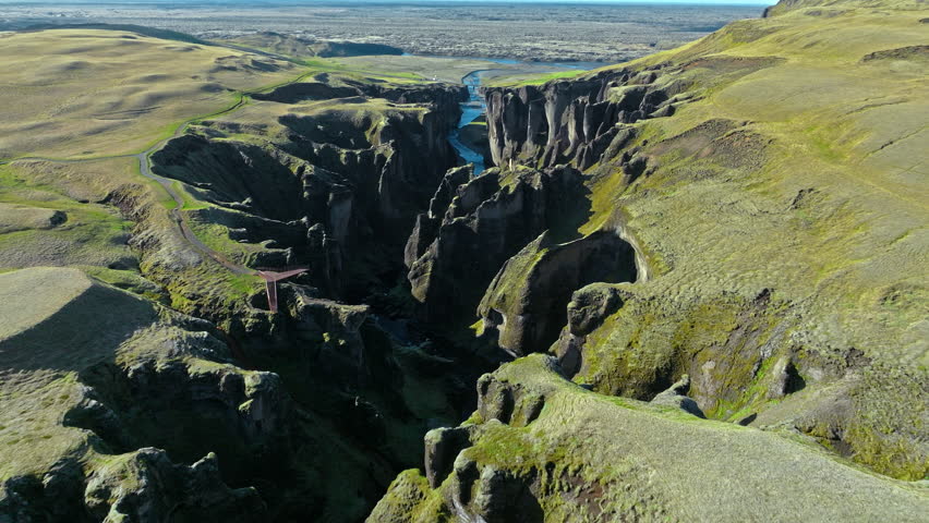 Tourist woman on viewing platform Fjadrargljufur canyon Iceland. 4K cinematic drone footage shows visitor overlooking mossy cliffs and winding river.