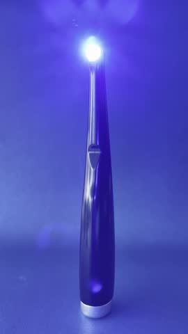 Close-up of a modern dental curing light with bright LED beam on dark background. Concept of dental equipment, tooth filling, and professional dentistry tools.
