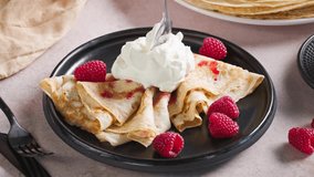 plate of freshly baked crepes decorated with raspberries. cook put whipped yogurt cream on pancakes with spoon for making delicious breakfast, sweet dessert closeup in kitchen - Powered by Shutterstock - Get 15% off with code: PIKWIZARD15