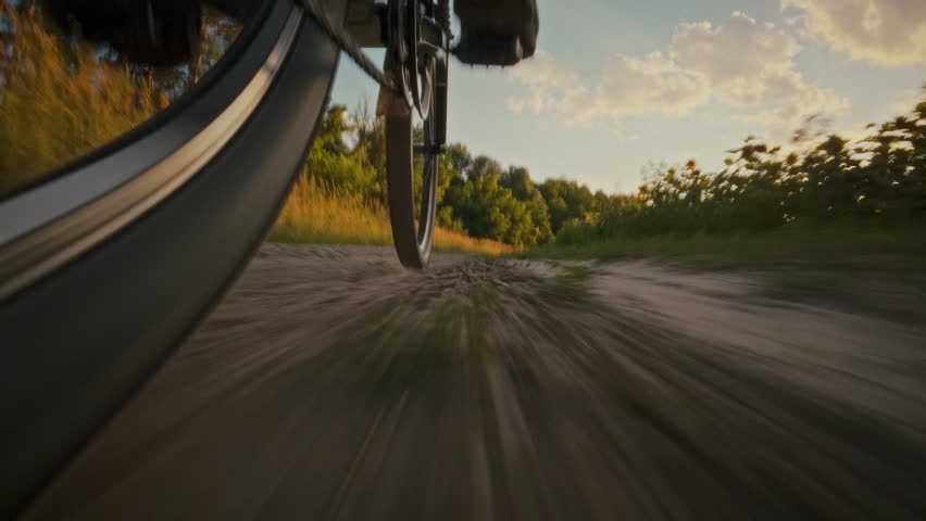 A cyclist rides along a dirt path, enjoying the fresh air and scenic views. The sun casts a warm glow on the landscape, highlighting the lush greenery on either side