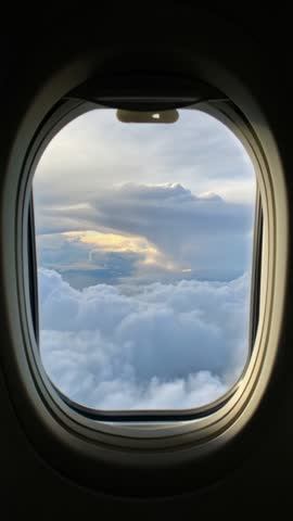 A View out of an airplane window onto a light blue sky and clouds and sunlight