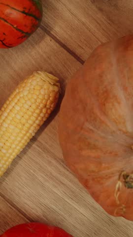 Different size pumpkins and vegetables lying on wooden background, rotating top view. Fall background with colorful various kinds mini pumpkins and vegetables. Vertical video
