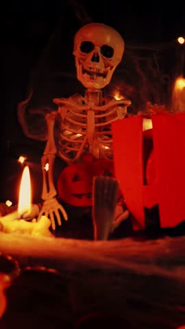 Horror Halloween concept. Word Halloween against dark spooky background with lighting candles, cobwebs, pumpkins scary faces and skeleton. Vertical video